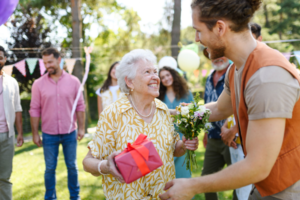 Garden birthday party for senior lady. Beautiful senior birthday woman receiving birthday wishes and gifts.