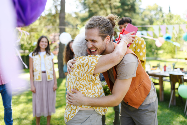 Garden birthday party for senior lady. Beautiful senior birthday woman receiving gift from grandson.