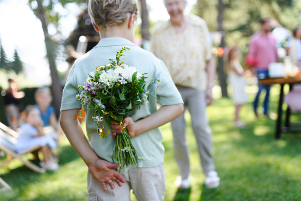 Beautiful senior birthday woman receiving flowers from grandson, grandchildren. Concept of garden birthday party for elderly woman.