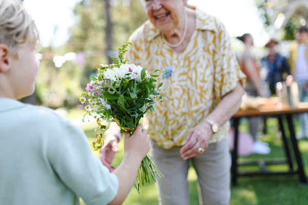 Beautiful senior birthday woman receiving flowers from grandson, grandkid. Concept of garden birthday party for elderly woman.