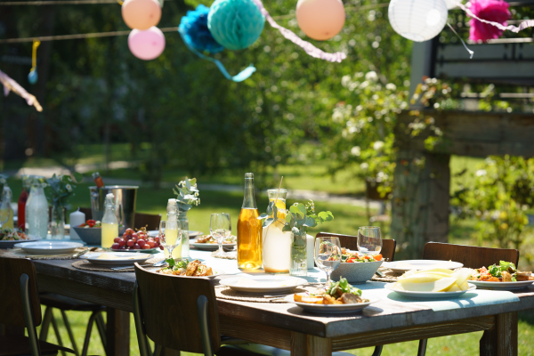 Close up shot of a set table at summer garden party, grilled food. Table setting with glasses, lemonade, delicate floral and paper decoration, and bottles of summer wine.