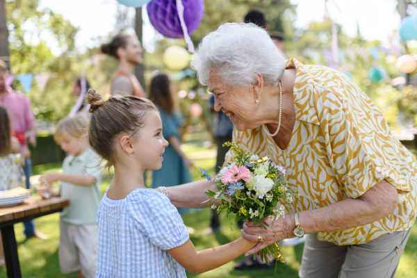 Garden birthday party for senior lady. Beautiful senior birthday woman receiving gift from granddaughter, hugging.