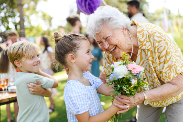 Garden birthday party for senior lady. Beautiful senior birthday woman receiving flowers from grandchildren.