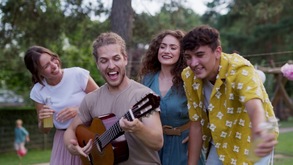 Handsome man playing at guitar for dancing friends at party. Friends and family dancing and having fun at a summer grill garden party.