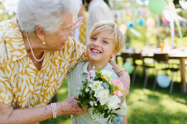 Garden birthday party for senior lady. Beautiful senior birthday woman receiving flowers from grandson.