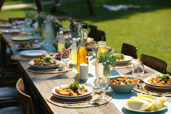 Close up shot of a set table at a summer garden party. Table setting with glasses, lemonade, fresh fruits and salad and the delicate floral decoration.