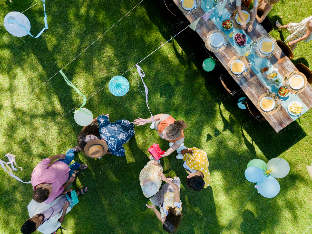 Top view of a garden party with decorations and a set table. The birthday girl greeting guests and receiving birthday wishes and gifts.