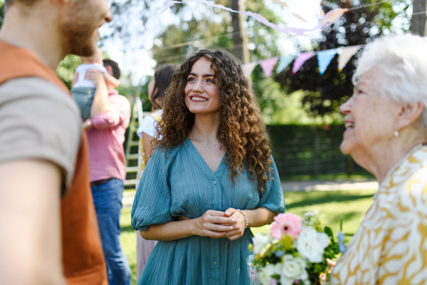 Grandparents giving flowers and present to granddaughter as surprise at birthday party. Friends and family reunite at garden party.