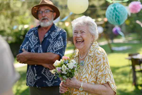 Garden birthday party for senior lady. Beautiful senior birthday woman receiving flowers as gift.