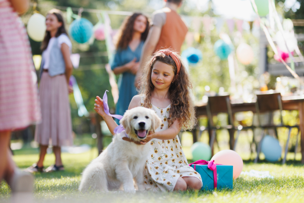 Garden birthday party for young girl. Beautiful birthday girl received a puppy as a birthday gift.