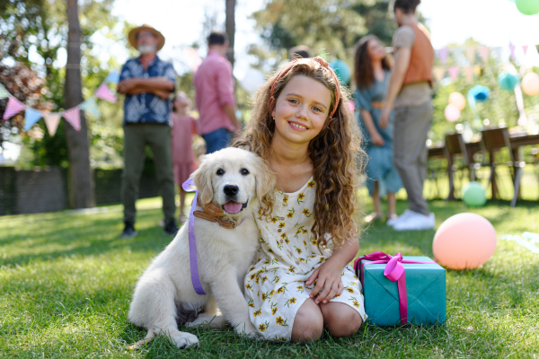 Garden birthday party for young girl. Beautiful birthday girl received a puppy as a birthday gift.