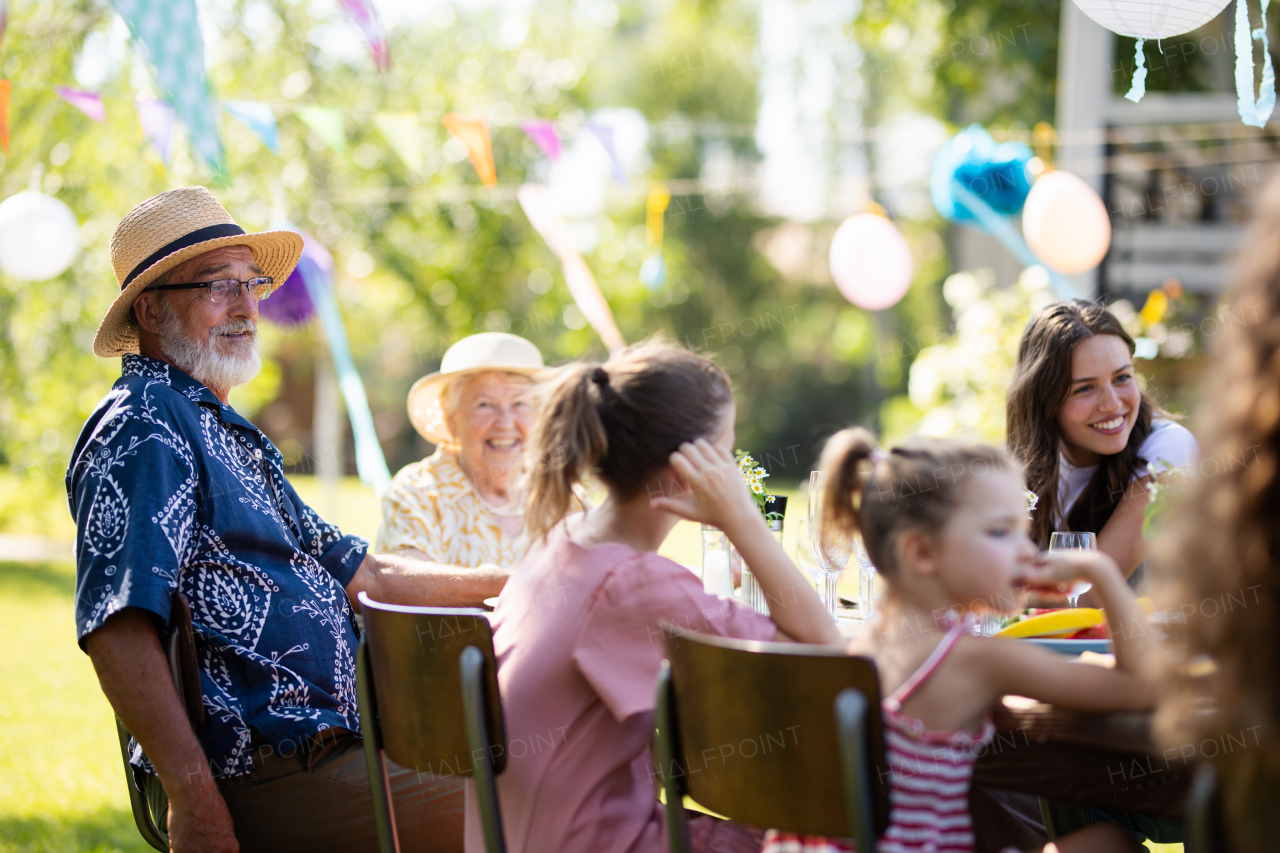 Family chatting having fun at the party table during a summer garden party. Grandfather sitting at head of table.