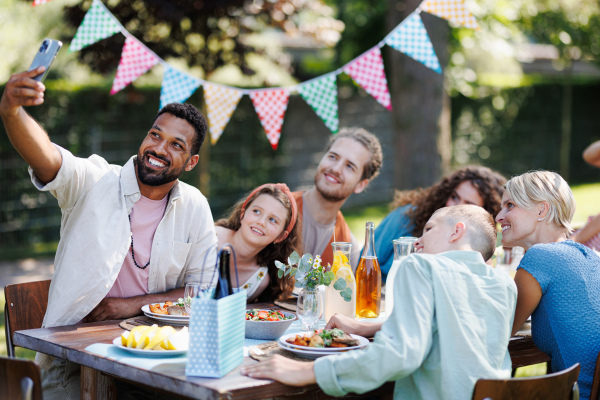 The whole family sitting at the table taking a group selfie at the family garden party. A family gathering to celebrate a birthday.