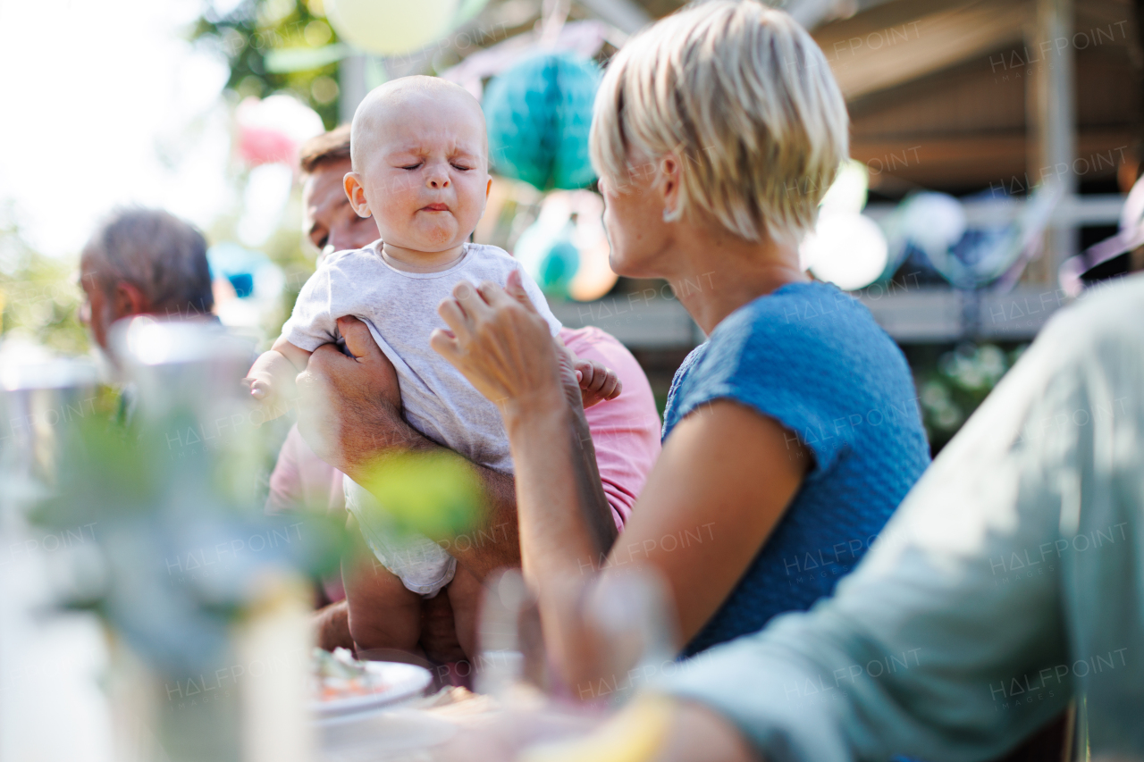 Cute baby eating something sour at summer garden party, making face.