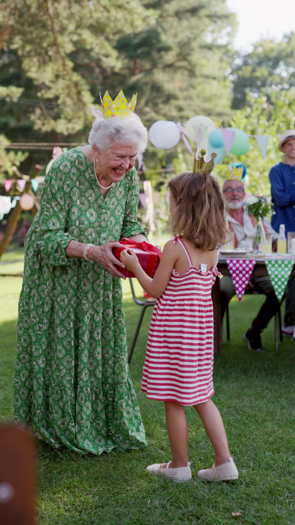 Garden birthday party for senior lady. Beautiful senior birthday woman receiving gifts from grandchildren.