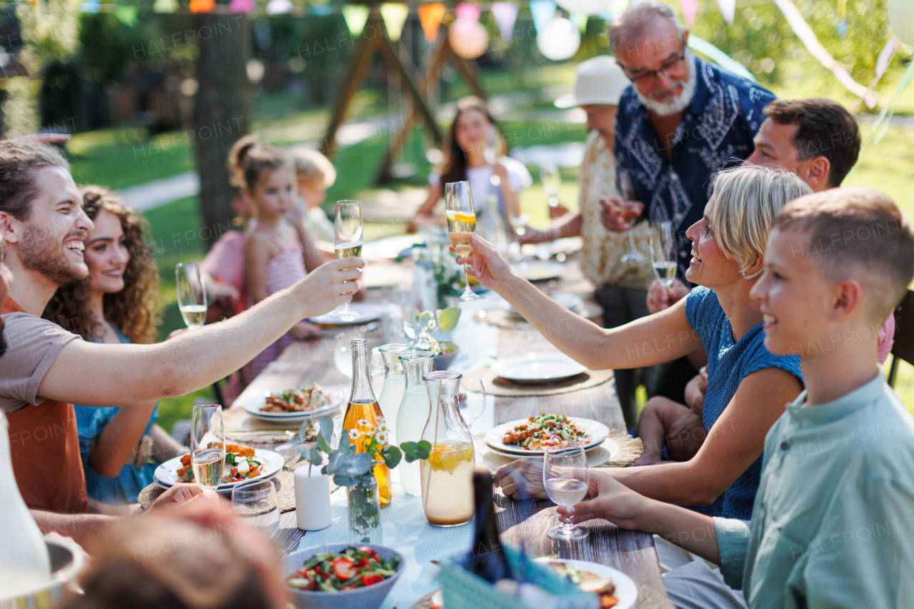 Family and friends clinking glasses at summer garden party. Celebratory toast at the table. Big family garden bbq.