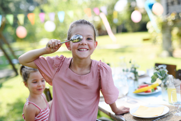 Girl covering eye with a spoon in front of her face. Friends are having fun at children's birthday party. Cousins having fun at a family garden party outdoors.