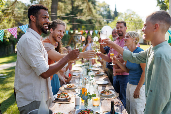 Group of friends clinking glasses at summer garden party. Celebratory toast at the table.