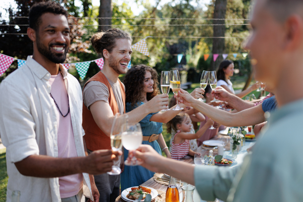 Friends clinking glasses at summer garden party. Celebratory toast at the table. Big family garden bbq.