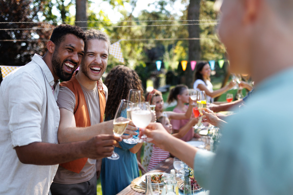 Friends clinking glasses at summer garden party. Celebratory toast at the table. Big family garden bbq.