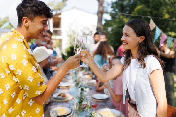 Friends clinking glasses at summer garden party. Celebratory toast at the table. Big family garden bbq.