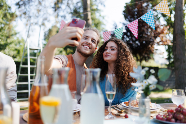 Portrait of couple taking selfie, sitting at the table with family and friends at the family garden party. A family gathering to celebrate a birthday.