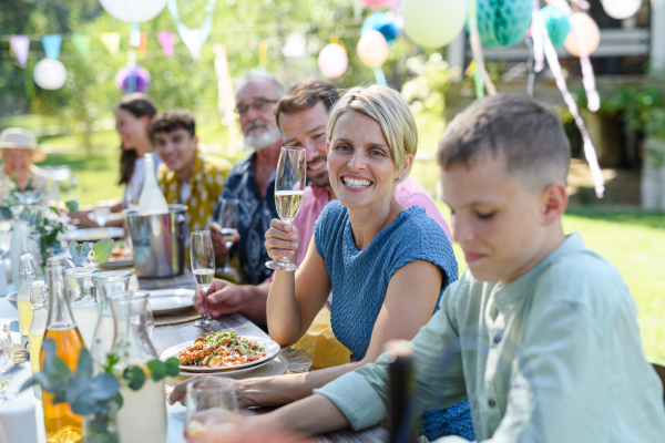 Family chatting, and having fun at party table during summer garden party. Beautiful woman toasting, cheering with glass with champagne.