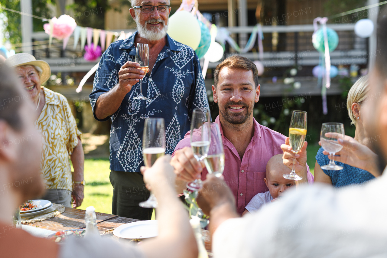 Big family clinking glasses at summer garden party. Celebratory toast at the table.