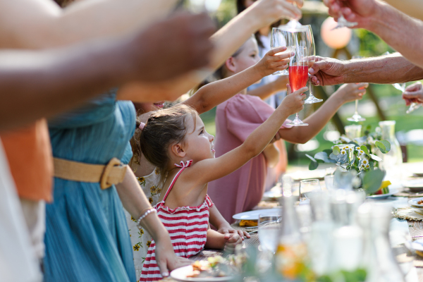 Family clinking glasses at summer garden party, kids clinking with nonalcoholic drink, lemonade. Celebratory toast at the table. Big family garden bbq.