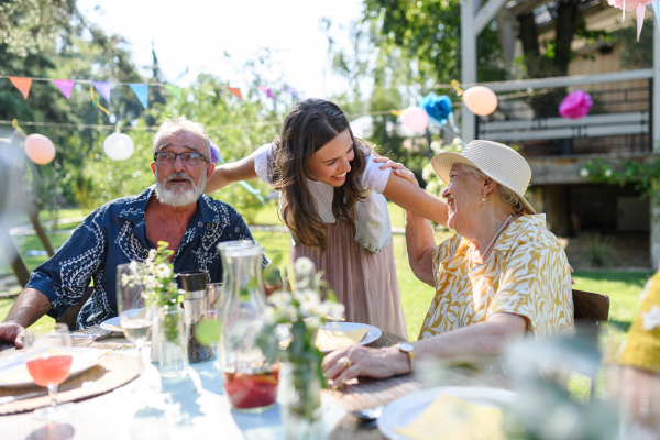 Mature granddaughter talking with grandparents, reunite after a long time. Family gathering at a garden party.