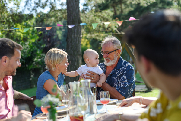 Cute baby playing with grandfather at summer garden party. The grandfather holding the baby boy in his arms and smiling.