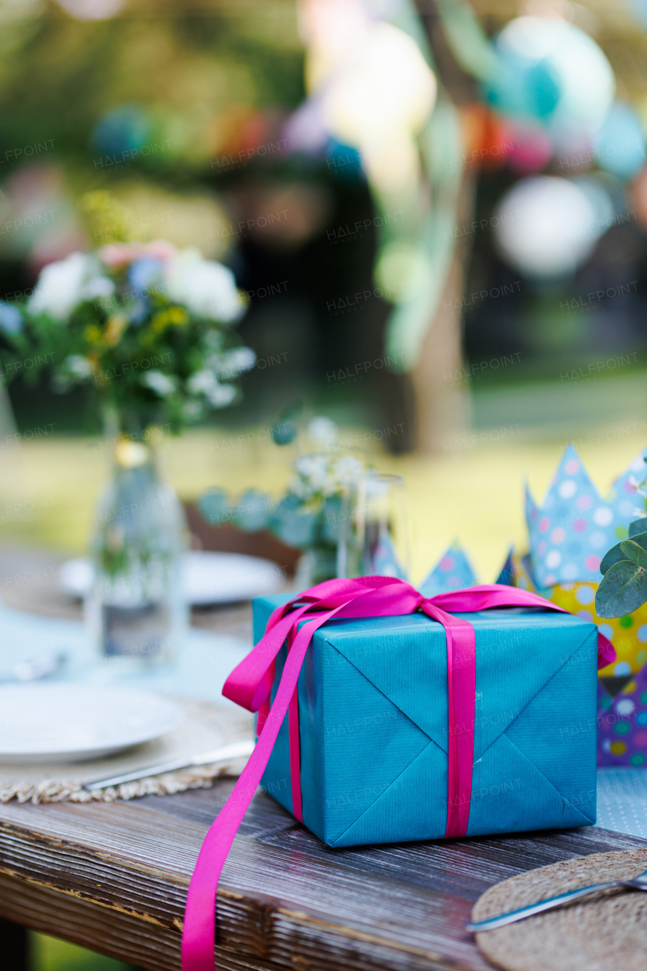 Close up of a birthday gift in blue wrapping paper with pink ribbon. Summer garden birthday party in a beautiful garden.