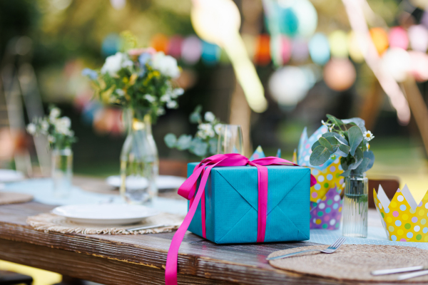 Close up of a birthday gift in blue wrapping paper with pink ribbon. Summer garden birthday party in a beautiful garden.