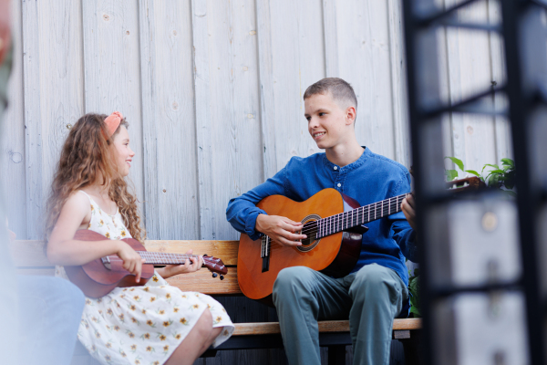 Boy and girl playing acustic guitars, making music together. Beautiful music by young teenagers. Sitting outdoors.