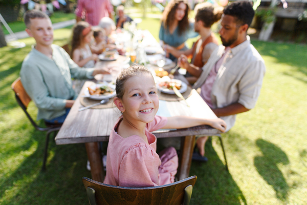 Portrait of girl sitting at the table with family and friends at the family garden party. A family gathering to celebrate a birthday.