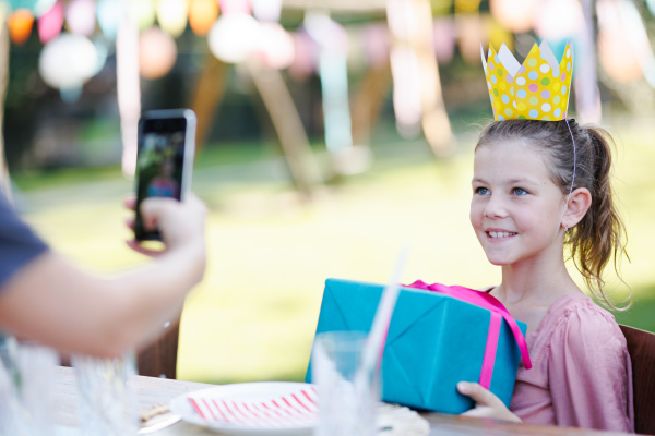 Beautiful birthday girl holding birthday gift posing for a photo. Garden birthday party for young girl.