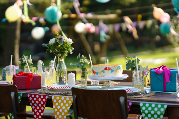 Shot of the birthday table with colorful decorations, birthday cake, and gifts. Inspiration for simple, tasteful birthday decoration for a garden party.