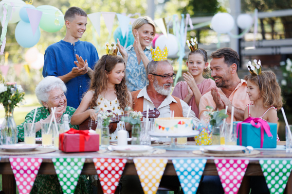 Garden birthday party for senior lady. Beautiful senior birthday woman receiving gift from granddaughter, family and friends. Birthday celebration with paper crowns.