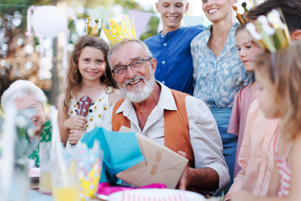 Family birthday garden party for senior man. Family sitting at the table having fun, little girl playing ukulele for the birthday man.