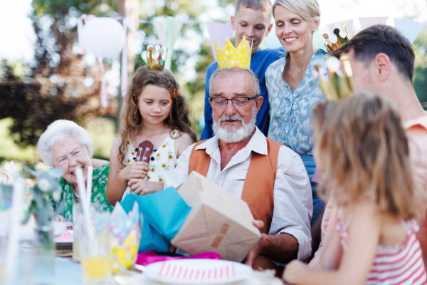 Family birthday garden party for senior man. Family sitting at the table having fun, little girl playing ukulele for the birthday man.