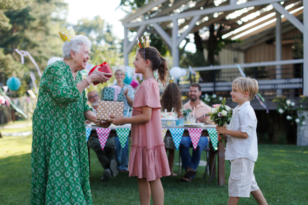 Garden birthday party for senior lady. Beautiful senior birthday woman receiving gift and flowers from grandchildren.