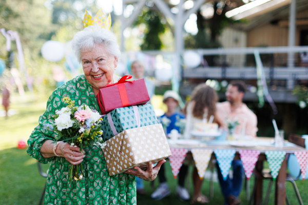 Portrit of senior birthday woman holding gifts and bouquet in hands. Garden birthday party for senior lady.