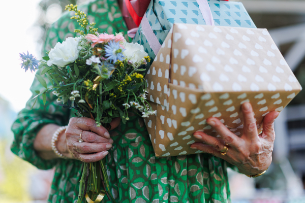 Close up of senior birthday woman holding gifts and bouquet in hands. Garden birthday party for senior lady.