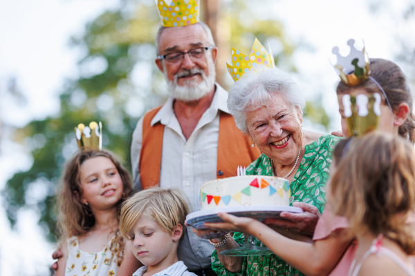 Garden birthday party for senior lady. Beautiful senior birthday woman receiving gift from granddaughter, family and friends. Birthday celebration with paper crowns.