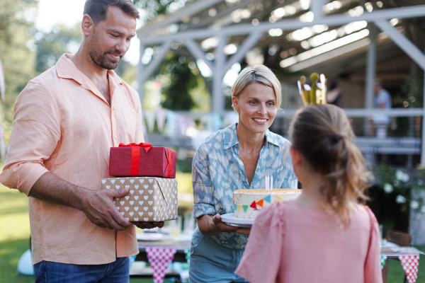 Garden birthday party with surprise for girl. Parents giving daughter presents, gifts and birthday cake as birthday surprise