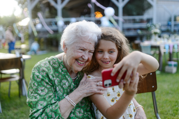 Young girl taking selfie photo with elderly grandmother at a garden party. Love and closeness between grandparent and grandchild.