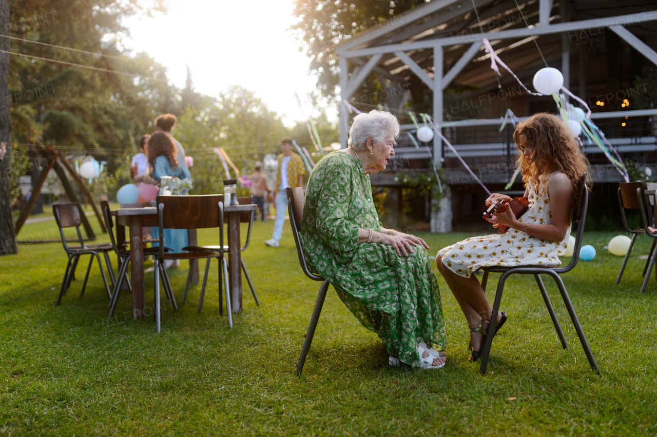 Girl playing on guitar for grandmother at garden party. Love and closeness between grandparent and grandchild.