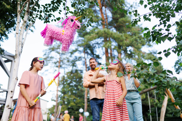 Two girls smashing, hitting pink pinata with a stick at birthday party. Children celebrating birthday at garden party. Children having fun and playing.