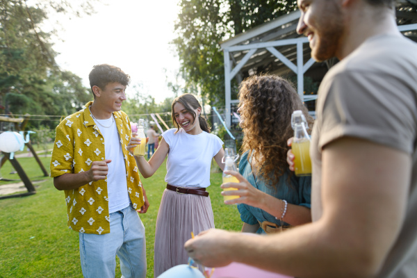 Friends and family talking and having fun at a summer grill garden party. People at the party dancing and laughing, holding glasses with drinks.