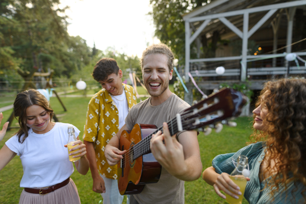 Handsome man playing at guitar for dancing friends at party. Friends and family dancing and having fun at a summer grill garden party.